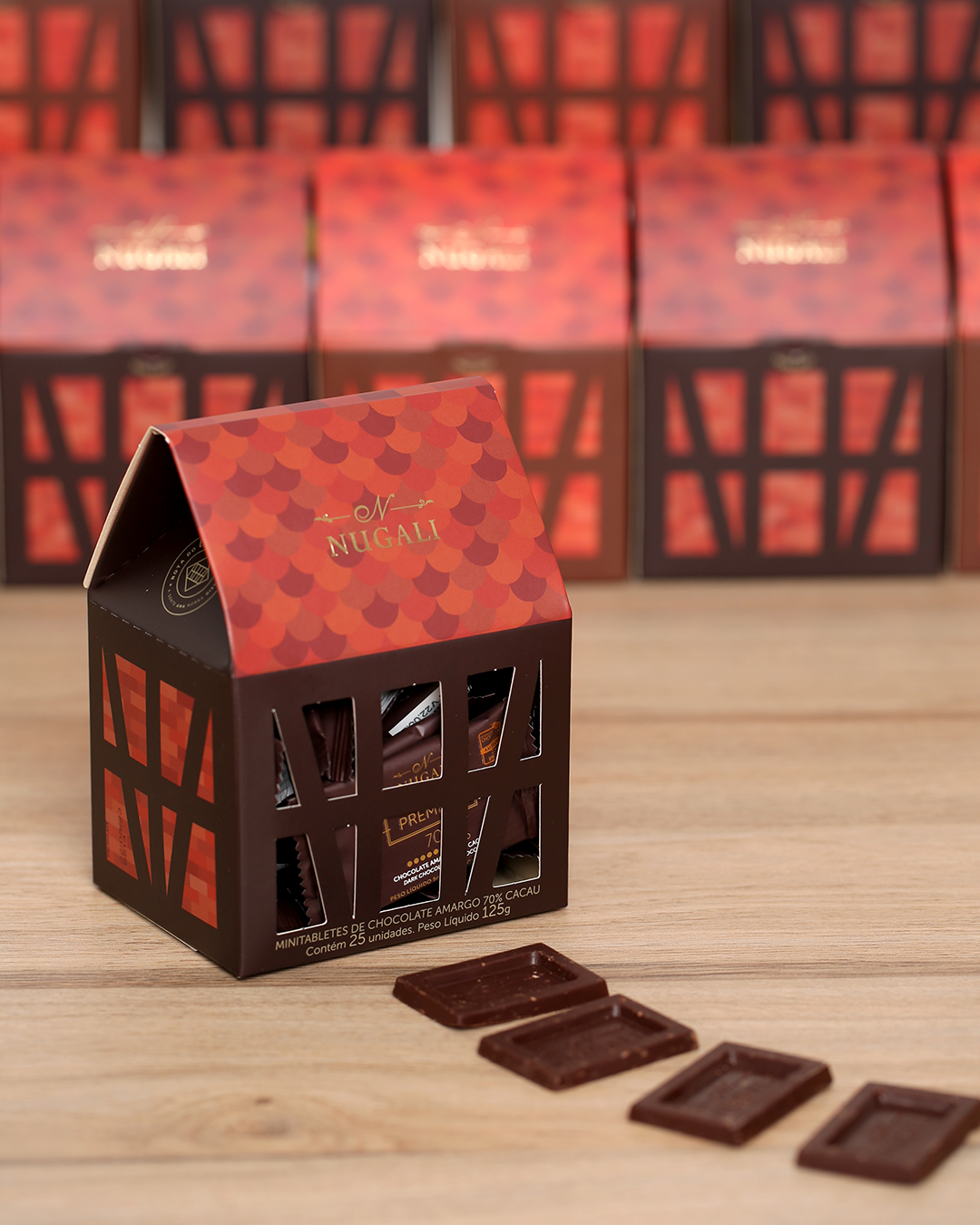 Caixinha Enxaimel com 25 mini tabletes de chocolate amargo embalados numa casa feita em papel que faz referência às peças de madeira da arquitetura enxaimel.